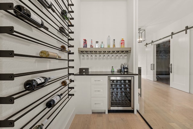 wine area featuring a barn door, bar, beverage cooler, and light hardwood / wood-style floors