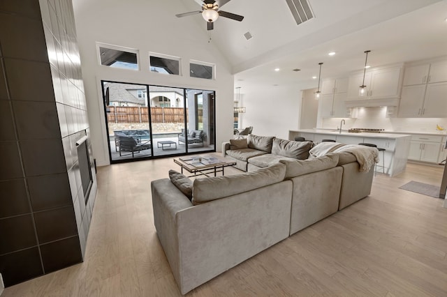 living room with ceiling fan, high vaulted ceiling, and light wood-type flooring