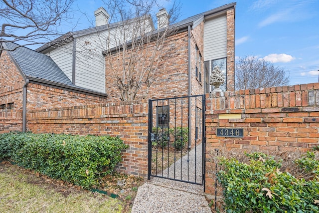 exterior space featuring brick siding, a chimney, fence, and a gate