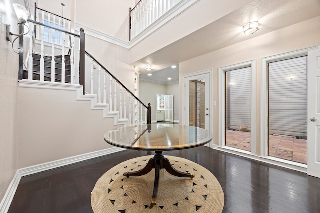 foyer entrance featuring baseboards, a towering ceiling, stairway, dark wood-type flooring, and crown molding