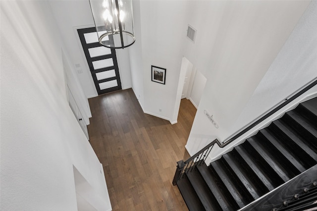 entrance foyer featuring a notable chandelier, a towering ceiling, wood finished floors, baseboards, and stairs