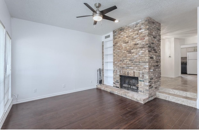 unfurnished living room with ceiling fan, a fireplace, a textured ceiling, dark hardwood / wood-style flooring, and built in shelves