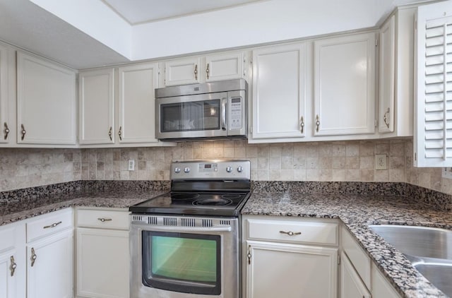 kitchen with sink, white cabinetry, dark stone countertops, stainless steel appliances, and tasteful backsplash