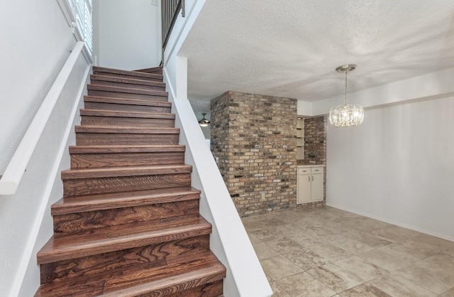 stairway featuring a chandelier, a textured ceiling, and brick wall