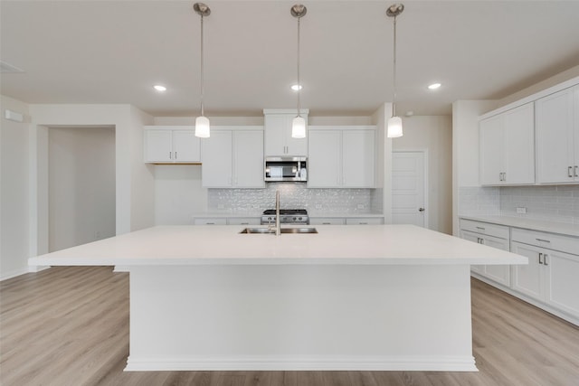 kitchen featuring white cabinetry, light hardwood / wood-style floors, an island with sink, and pendant lighting