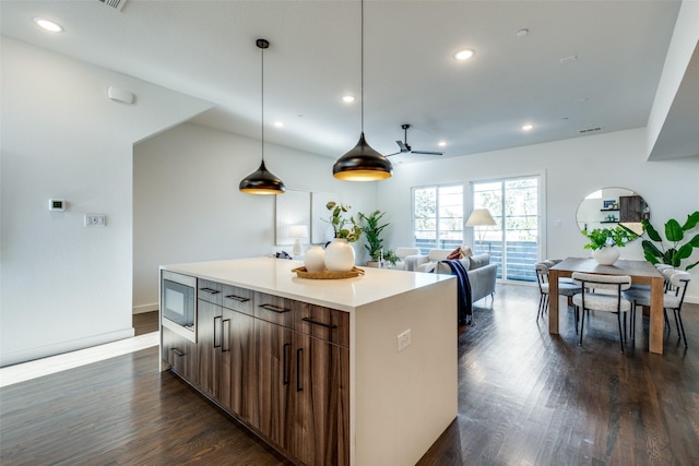 kitchen featuring stainless steel microwave, dark wood finished floors, a kitchen island, recessed lighting, and light countertops