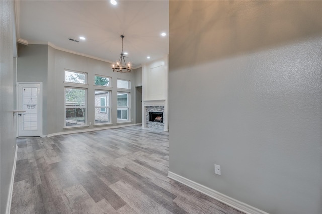 unfurnished living room featuring a stone fireplace, a towering ceiling, a chandelier, crown molding, and light hardwood / wood-style flooring