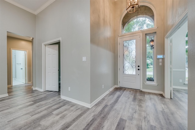 entryway with crown molding, a towering ceiling, a chandelier, and light wood-type flooring