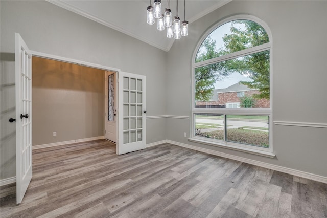 empty room featuring vaulted ceiling, a chandelier, crown molding, light wood-type flooring, and french doors