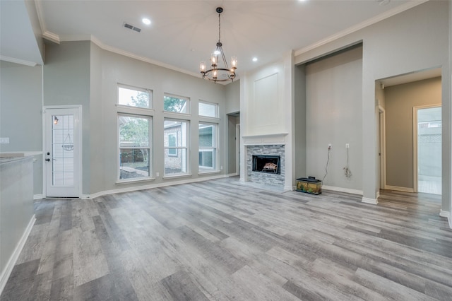 unfurnished living room with ornamental molding, a stone fireplace, a notable chandelier, and light wood-type flooring