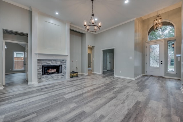 unfurnished living room with light wood-type flooring, ornamental molding, a notable chandelier, a towering ceiling, and a fireplace