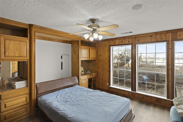 bedroom with wooden walls, a textured ceiling, multiple windows, and light wood-type flooring