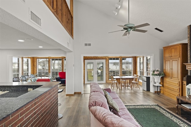 living room with french doors, wood-type flooring, high vaulted ceiling, a textured ceiling, and ceiling fan