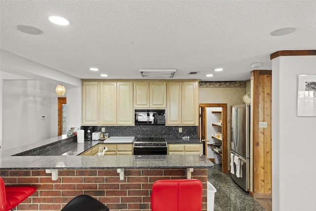 kitchen with a kitchen bar, a textured ceiling, range with electric stovetop, stainless steel fridge, and kitchen peninsula