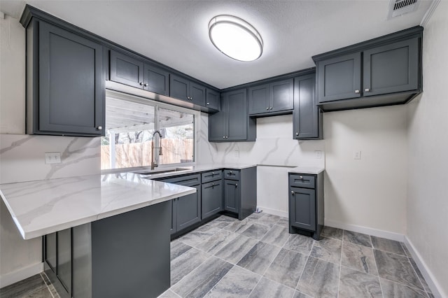 kitchen featuring tasteful backsplash, sink, gray cabinetry, kitchen peninsula, and light stone countertops