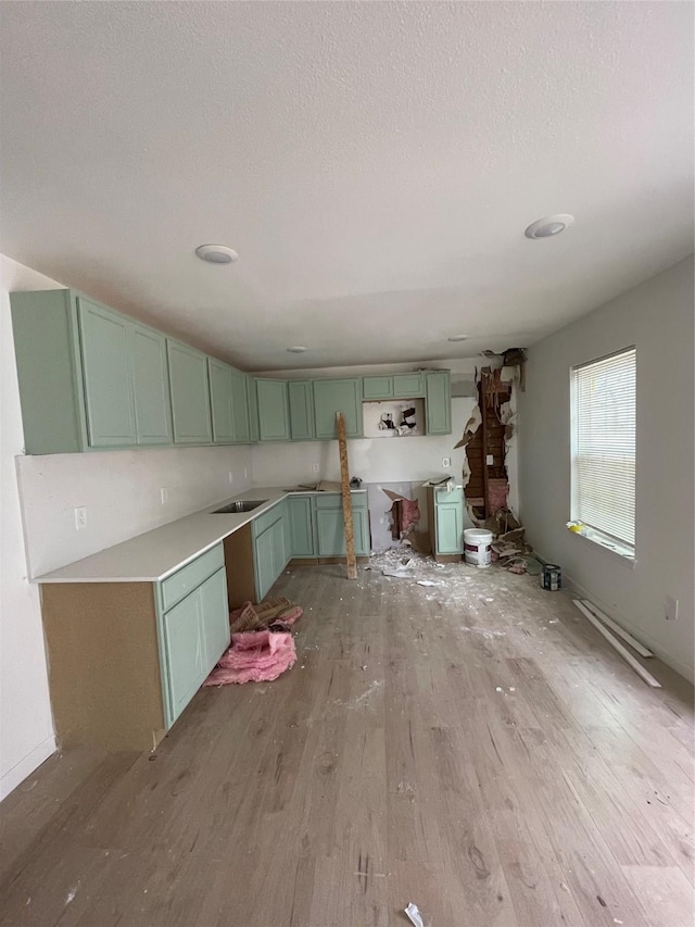 kitchen with sink, green cabinets, a textured ceiling, and light hardwood / wood-style flooring