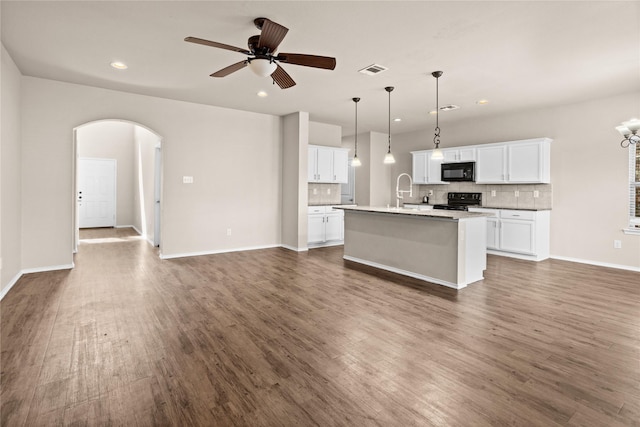 kitchen featuring decorative light fixtures, white cabinets, black appliances, dark wood-type flooring, and a center island with sink