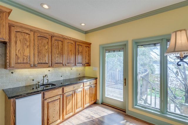 kitchen featuring sink, light wood-type flooring, ornamental molding, dark stone counters, and decorative backsplash