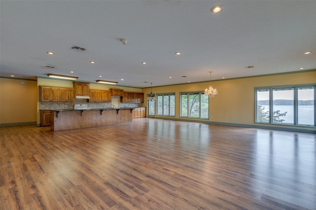 unfurnished living room with a water view, ornamental molding, a chandelier, and light hardwood / wood-style flooring