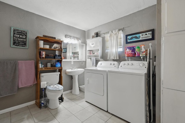 washroom featuring light tile patterned floors, laundry area, separate washer and dryer, a sink, and baseboards