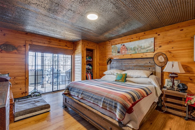bedroom featuring wood walls, access to exterior, and light wood-type flooring