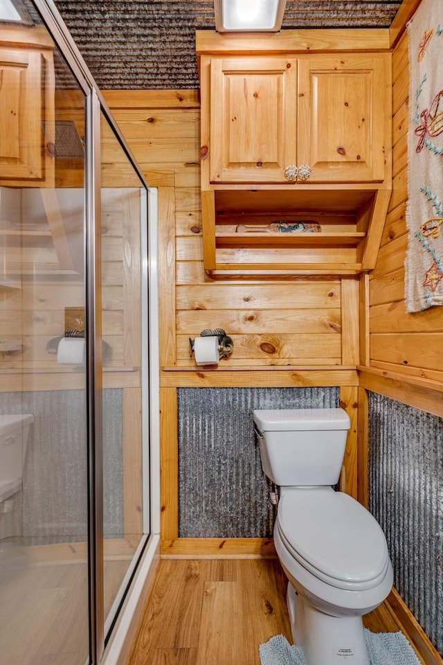 bathroom with wooden walls, wood-type flooring, toilet, and a shower with shower door