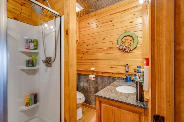 bathroom featuring wooden walls, vanity, toilet, and a shower with door