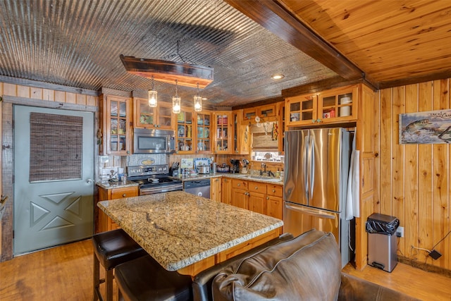 kitchen with appliances with stainless steel finishes, wood walls, sink, hanging light fixtures, and light hardwood / wood-style floors