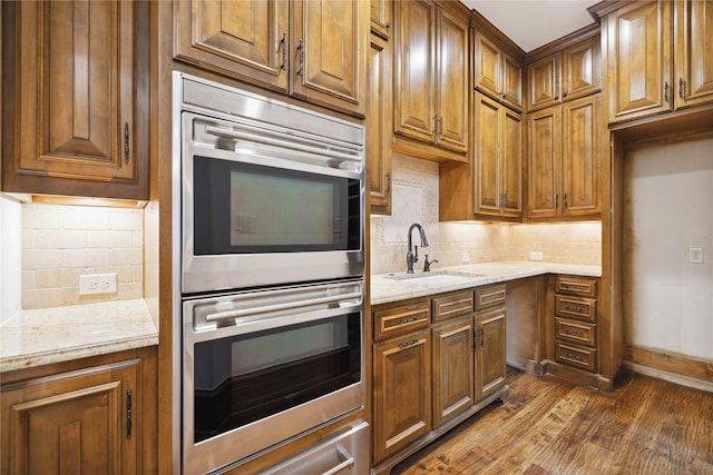 kitchen with dark wood-type flooring, sink, tasteful backsplash, double oven, and light stone countertops