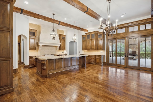 kitchen featuring premium range hood, hanging light fixtures, backsplash, light stone countertops, and a center island with sink