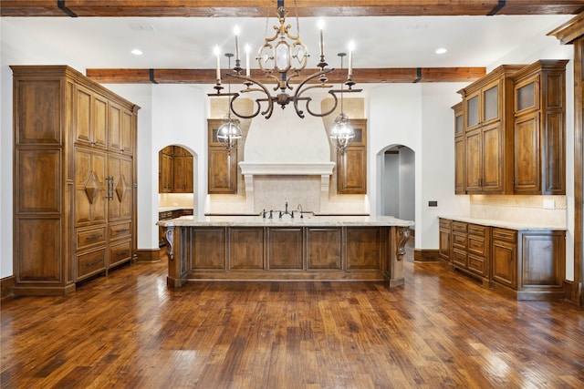 kitchen with light stone counters, decorative light fixtures, a kitchen island with sink, and custom exhaust hood