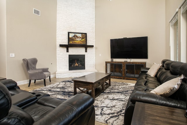 living room with hardwood / wood-style flooring, a stone fireplace, and a high ceiling