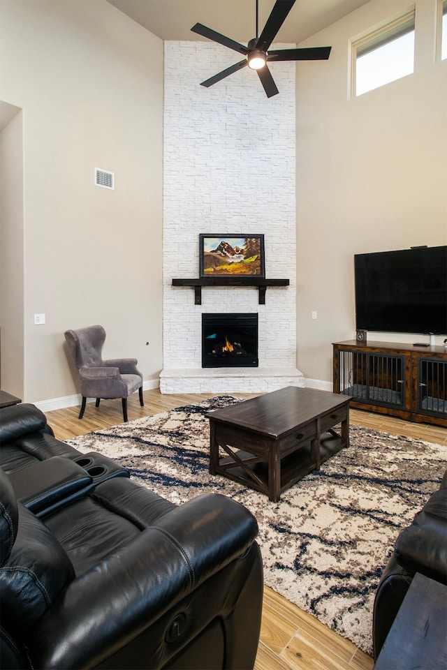 living room featuring ceiling fan, a towering ceiling, a fireplace, and light hardwood / wood-style floors