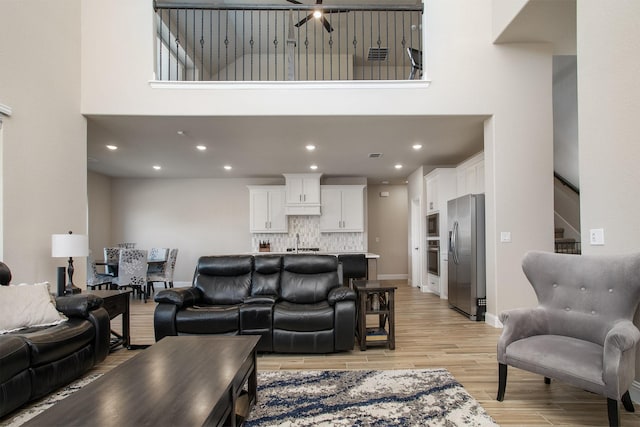 living room with a towering ceiling, sink, and light hardwood / wood-style flooring