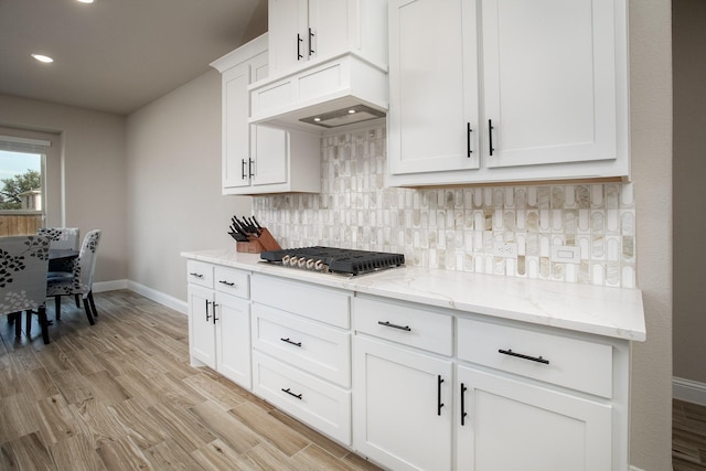 kitchen featuring stainless steel gas stovetop, white cabinets, backsplash, light stone countertops, and light hardwood / wood-style flooring