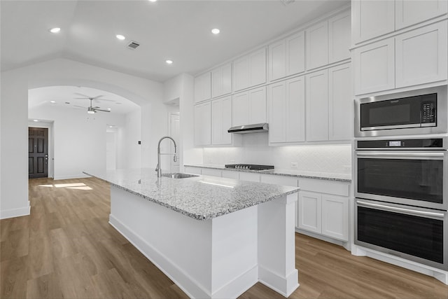 kitchen featuring arched walkways, a sink, visible vents, light wood-type flooring, and built in microwave