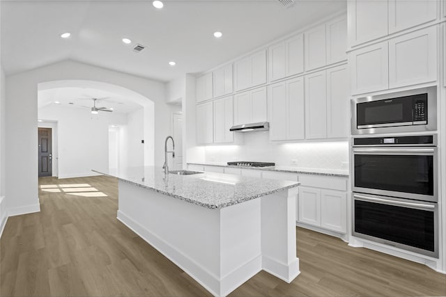 kitchen with ventilation hood, built in microwave, double oven, arched walkways, and a sink