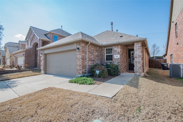 view of front of home with driveway, a shingled roof, central AC unit, an attached garage, and brick siding