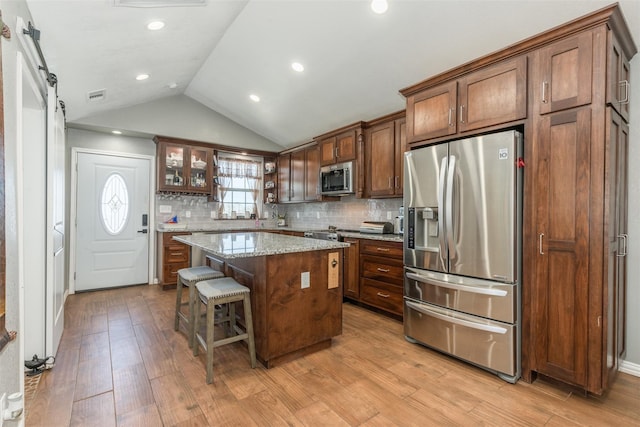 kitchen featuring appliances with stainless steel finishes, a kitchen bar, light stone countertops, a center island, and a barn door