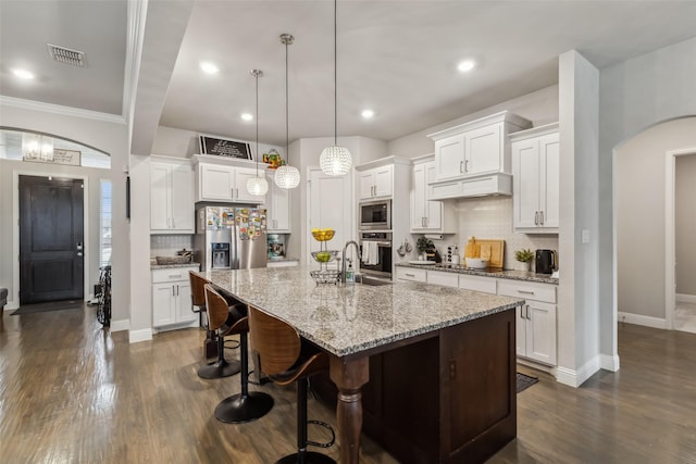 kitchen featuring pendant lighting, stainless steel appliances, an island with sink, white cabinets, and a kitchen bar