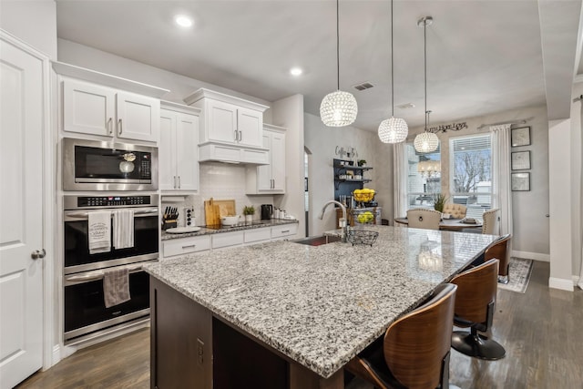 kitchen with decorative light fixtures, an island with sink, sink, white cabinets, and dark wood-type flooring