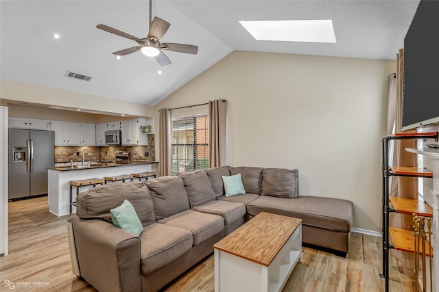 living room featuring light hardwood / wood-style flooring, lofted ceiling with skylight, and ceiling fan