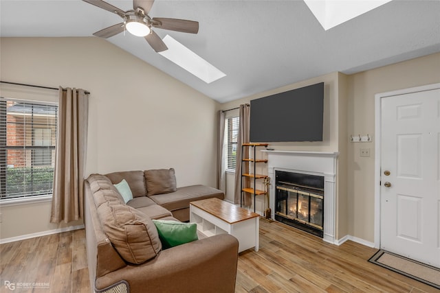 living room with ceiling fan, vaulted ceiling with skylight, light hardwood / wood-style floors, and a wealth of natural light