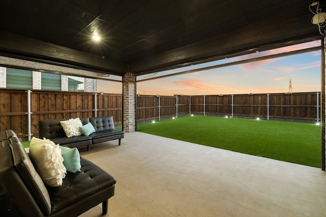 patio terrace at dusk featuring a fenced backyard, a lawn, and an outdoor living space