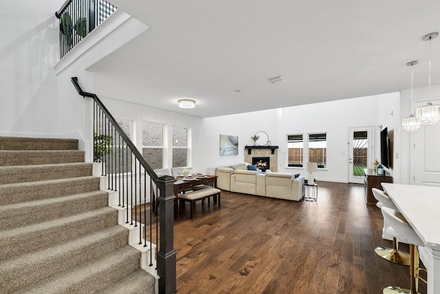 living area featuring a notable chandelier, a premium fireplace, visible vents, stairs, and dark wood-style floors