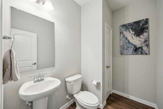 half bathroom with wood finished floors, a sink, toilet, and baseboards