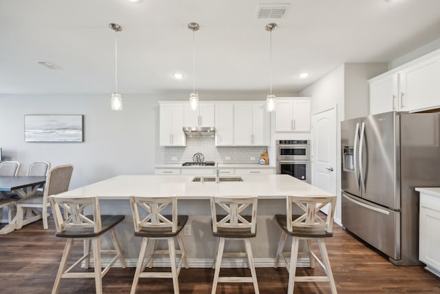 kitchen with a center island with sink, appliances with stainless steel finishes, light countertops, and decorative light fixtures