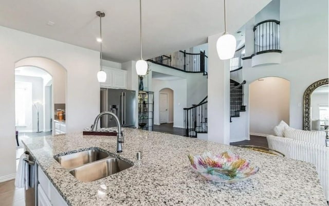 kitchen with arched walkways, stainless steel appliances, white cabinetry, a sink, and light stone countertops