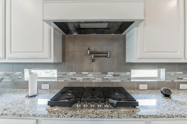 details with premium range hood, stainless steel gas stovetop, white cabinetry, and light stone counters