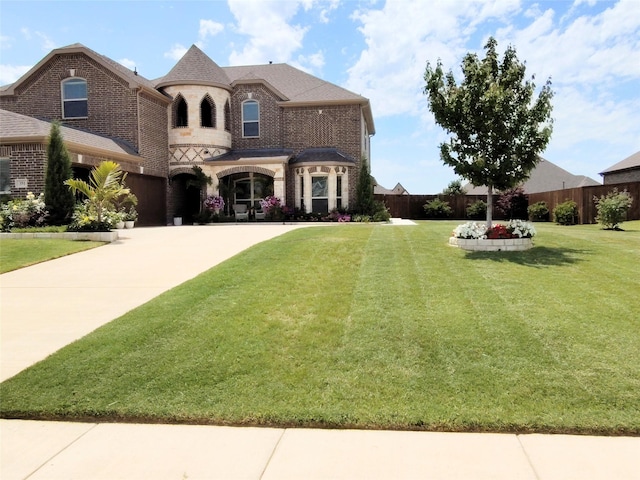 french country home with concrete driveway, brick siding, a front yard, and stone siding